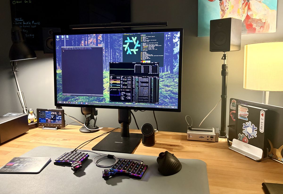A desk setup with monitor, keyboard, and two laptops in a stand to the side.