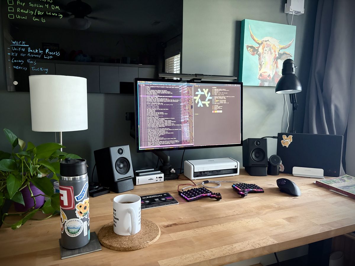 A wooden computer desk with a monitor, keyboard, speakers and other items going on it