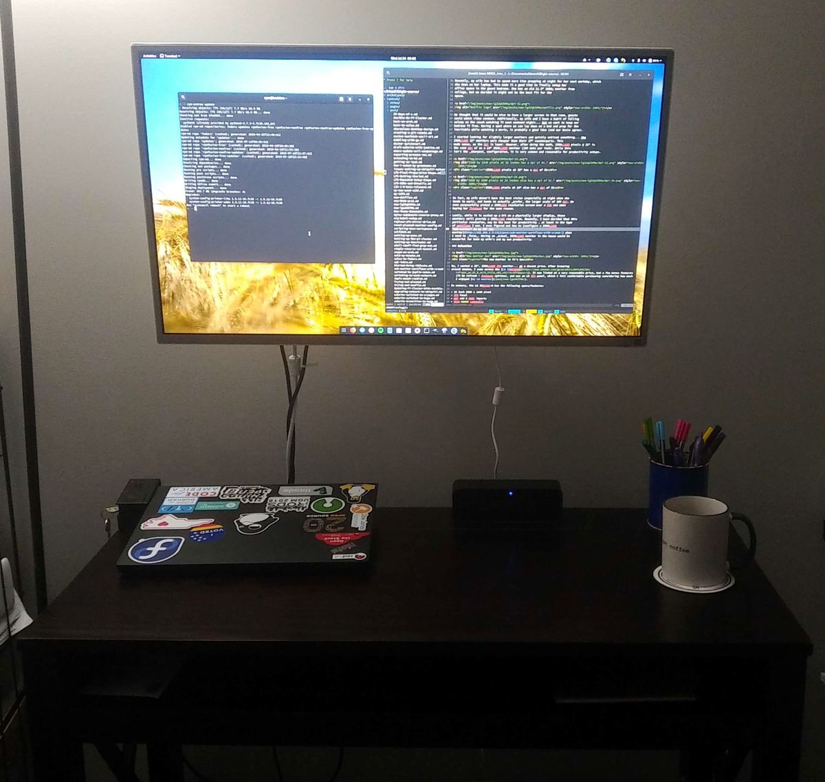 A simple small computer desk, with a docked laptop and a wall mounted monitor