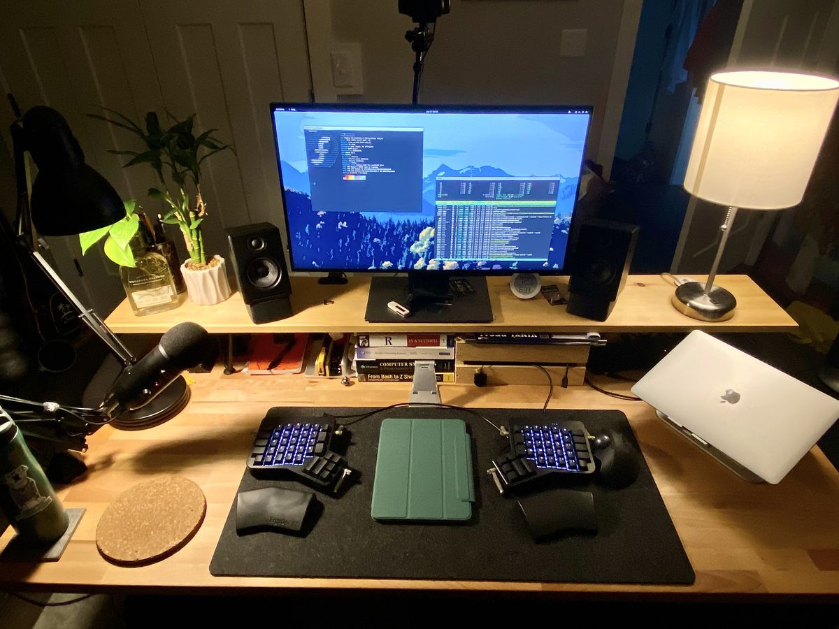 A wooden computer desk with warm light lamps, a monitor, and split keyboard