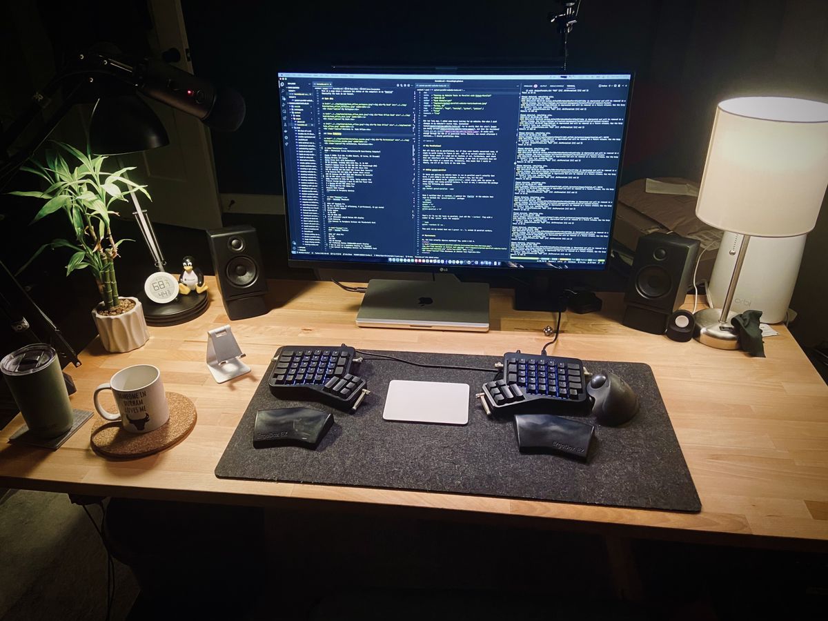 A center look of a wooden computer desk with a large monitor with code and a split keyboard