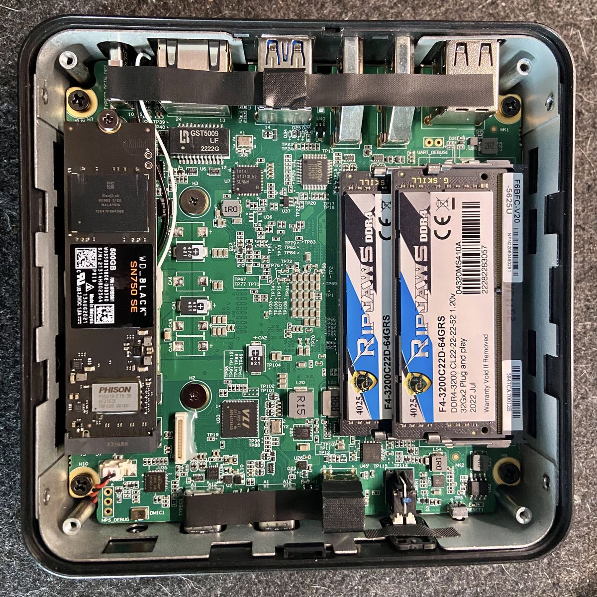 The insides of a square mini PC, showing an nvme drive on the left and to sticks of laptop RAM on the right