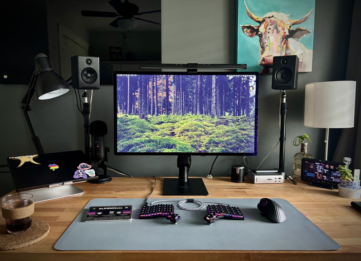 A wooden computer desk with a monitor, keyboard, speakers and other items going on it