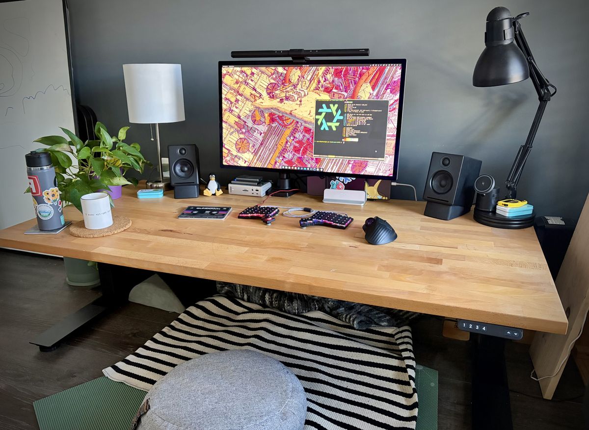 A wooden computer desk with a monitor, keyboard, speakers and other items going on it