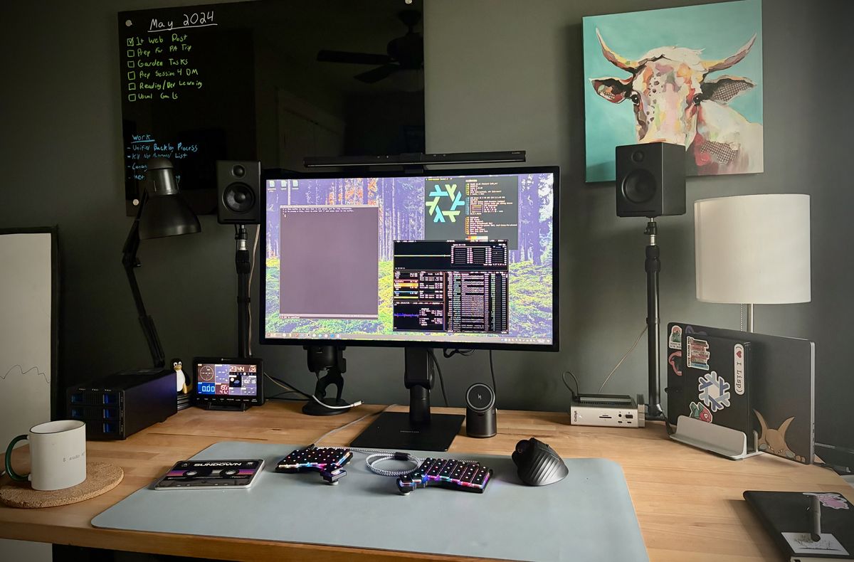 A wooden computer desk with a monitor, keyboard, speakers and other items going on it